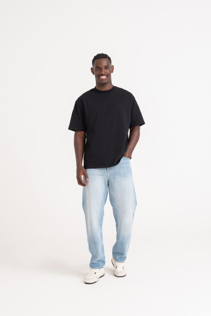 Model with one hand in their pocket wearing a black oversized t-shirt.